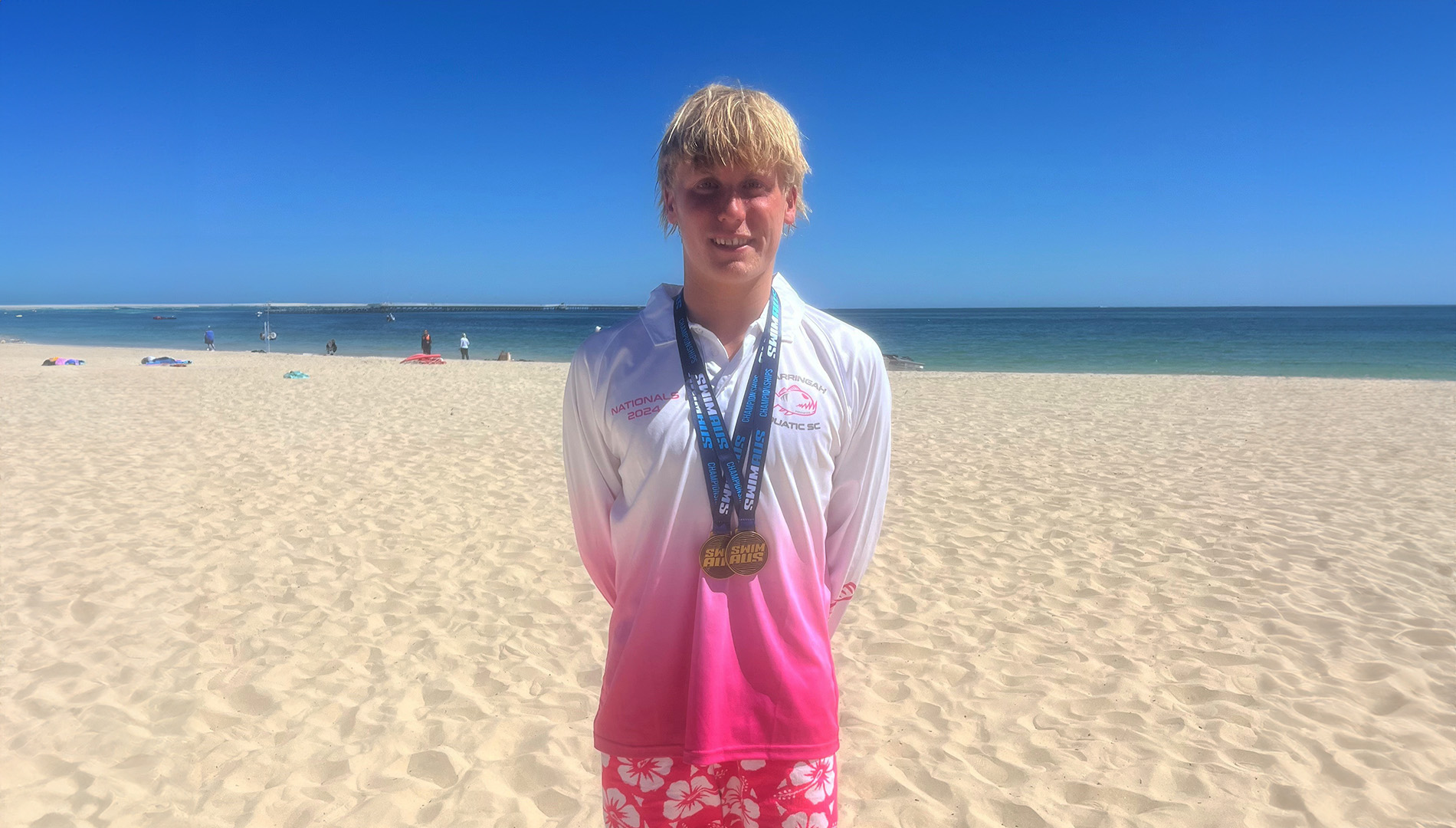 Luke standing on beach with medals.